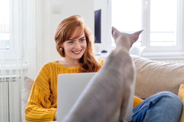 Free photo young beautiful woman doing online work at home beautiful sphynx cat distracting owner from work