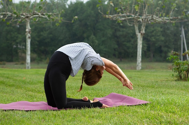 Young beautiful woman doing yoga exercise in green park. Healthy lifestyle and fitness concept.