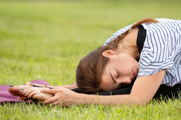 Young beautiful woman doing yoga exercise in green park