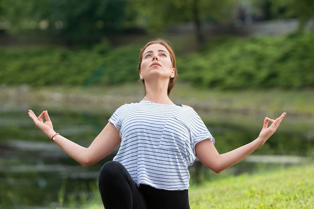 Giovane bella donna che fa esercizio di yoga nel parco verde