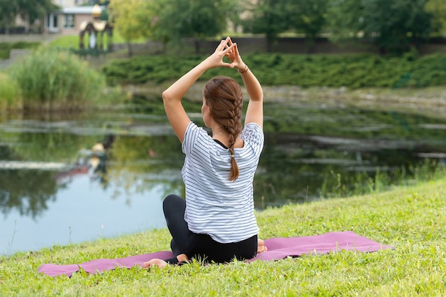 Giovane bella donna che fa esercizio di yoga nel parco verde