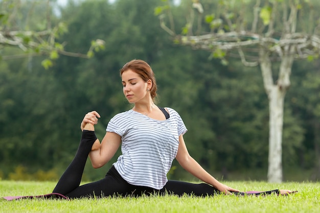 Молодая красивая женщина делает упражнения йоги в зеленом парке