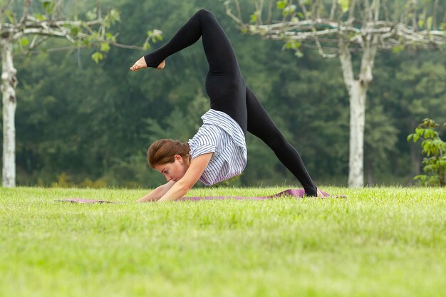 Young beautiful woman doing yoga exercises in green park