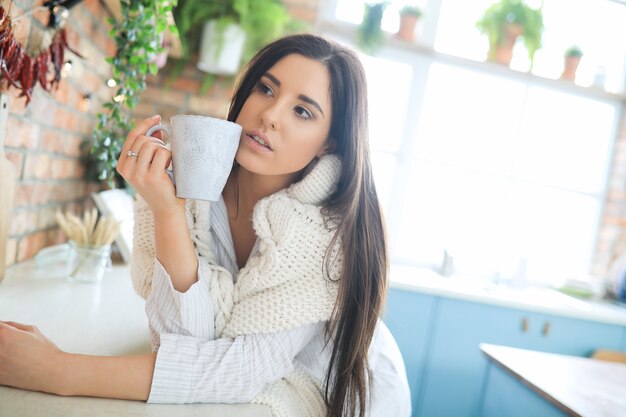 Young beautiful woman drinking a hot drink in the kitchen