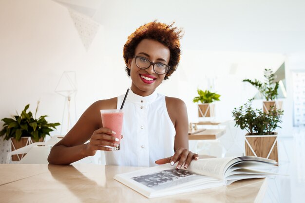 カフェで休んで笑顔スムージーを飲む若い美しい女性