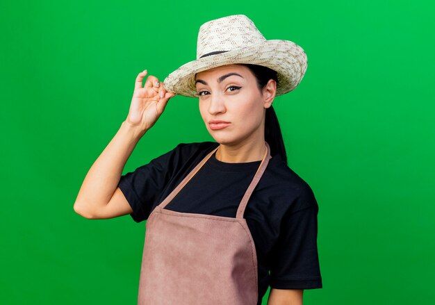 Giardiniere della giovane bella donna in grembiule e cappello con la faccia seria