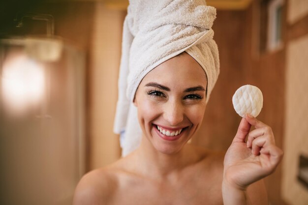 Young beautiful woman holding a cotton pad and looking at camera in the bathroom