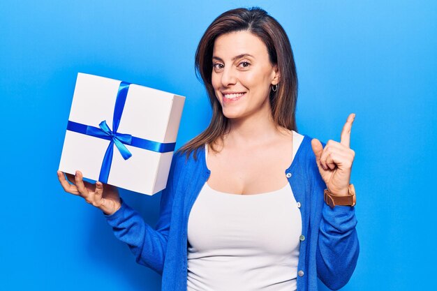 Young beautiful woman holding gift smiling happy pointing with hand and finger to the side