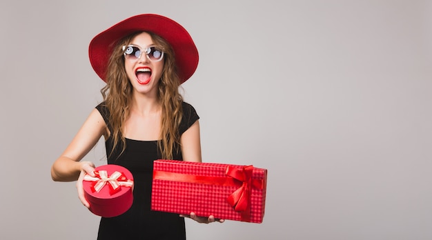 Young beautiful woman holding presents, black dress, red hat, sunglasses, happy, smiling, sexy, elegant, gift boxes, celebrating, positive, emotional