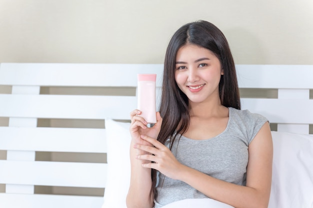 Young beautiful woman holding and skin lotion in her hand and smiling with happiness