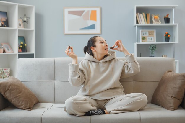 幸せで前向きなリラックスしたクッキーを食べる家のインテリアのソファに座っている家庭服を着た若い美しい女性