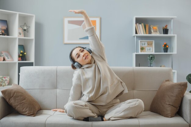 Free Photo young beautiful woman in home clothes sitting on a couch at home interior with headphones happy and positive relaxing stretching herself making exercises