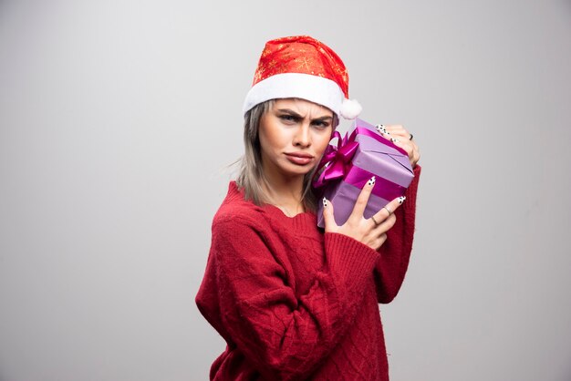 Young beautiful woman hugging her gift on gray background.