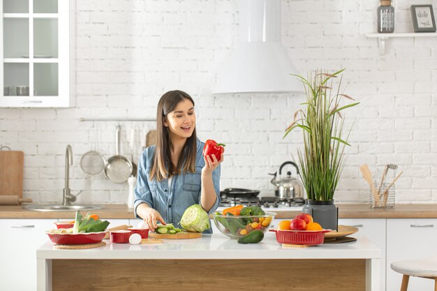 若い美しい女性が台所で様々な野菜のサラダを準備しています。