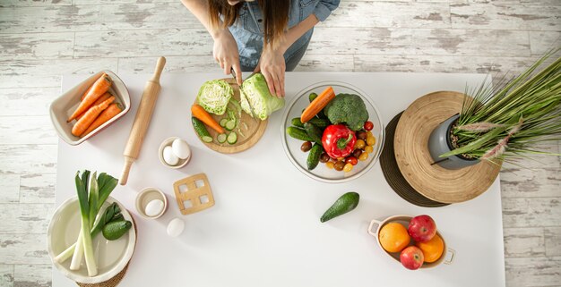 若い美しい女性が台所で様々な野菜のサラダを準備しています。