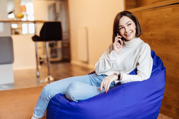 Молодая красивая женщина сидит в ярком фиолетовом кресле с помощью телефона