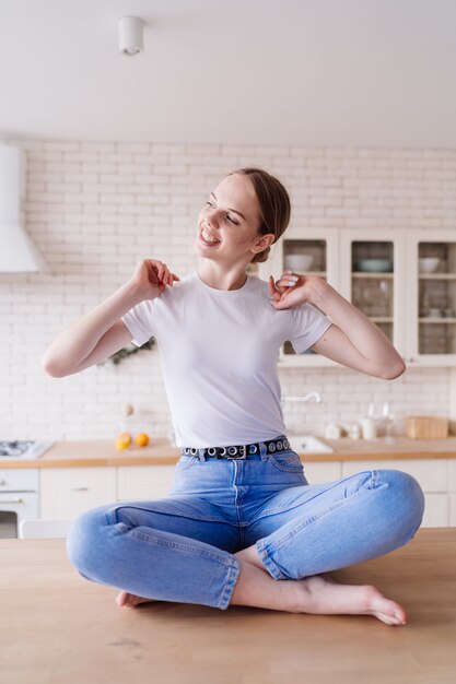 Молодая красивая женщина в джинсах и футболке позирует за кухонным столом