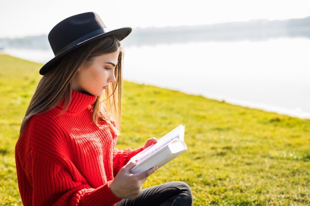 Young beautiful woman lays on green field and reads book.