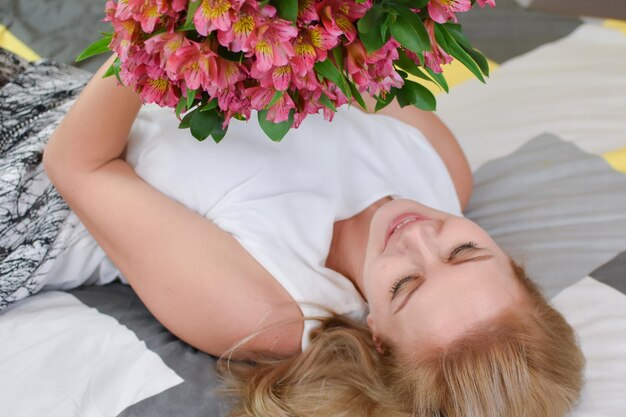 Young beautiful woman lies on bed with a bouquet of fresh flowers