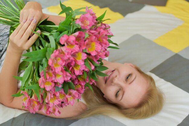 Young beautiful woman lies on bed with a bouquet of fresh flowers