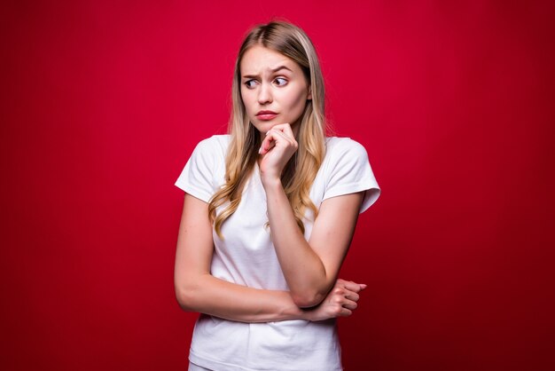 Young beautiful woman looking confident  smiling with crossed arms and hand raised on chin standing over isolated red wall. Thinking positive.