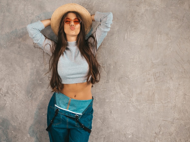 Young beautiful woman looking . Trendy girl in casual summer overalls clothes and hat. Making duck face