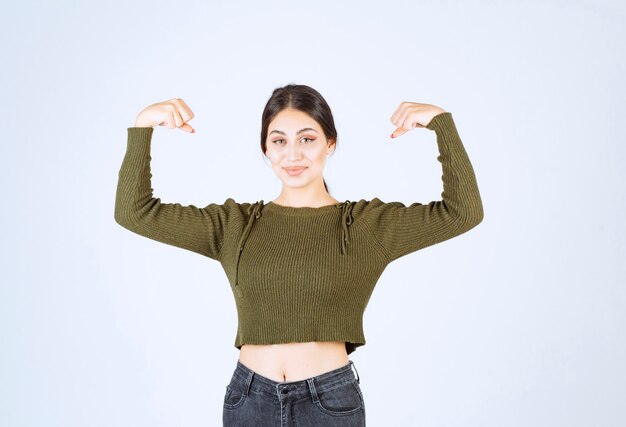 A young beautiful woman model showing her muscles over white wall