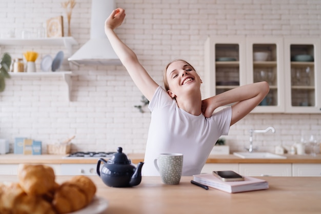 朝、キッチンでお茶を飲みながらストレッチする若い美しい女性