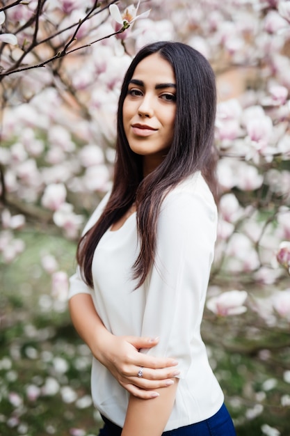 Giovane bella donna vicino all'albero di fioritura della magnolia. giovane donna sveglia vicino all'albero di magnolia