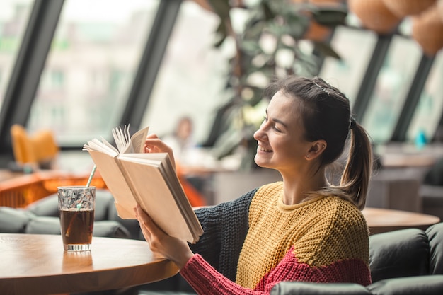 Молодая красивая женщина в оранжевом свитере читает интересную книгу в кафе