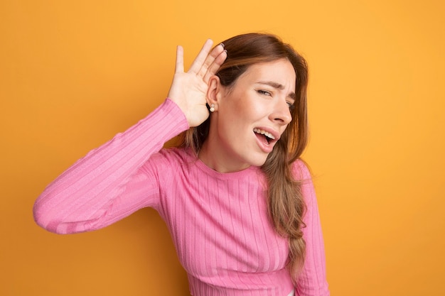 Free photo young beautiful woman in pink top holding hand over her ear trying to listen to gossips