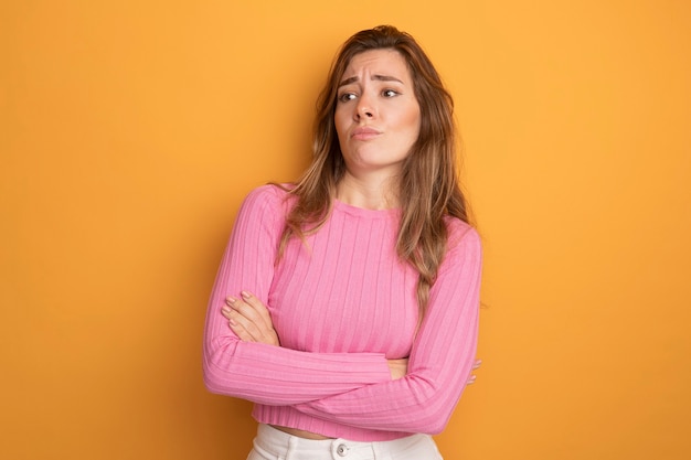 Free photo young beautiful woman in pink top looking aside displeased with arms crossed