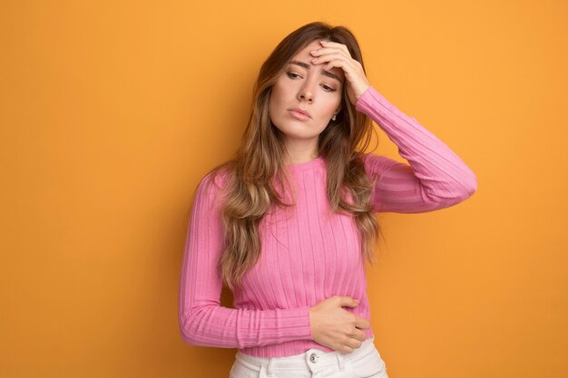 Young beautiful woman in pink top looking down stressed and worried standing over orange