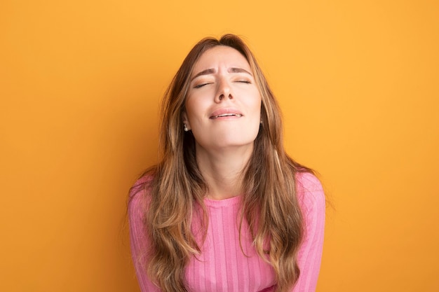 Young beautiful woman in pink top tired and bored with eyes closed standing over orange