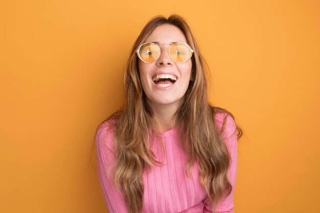 Young beautiful woman in pink top wearing glasses happy and cheerful laughing out 