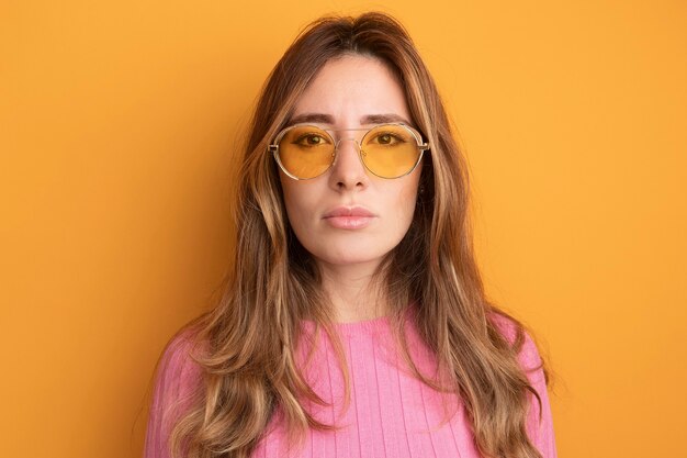 Young beautiful woman in pink top wearing glasses looking at camera with serious confident expression 