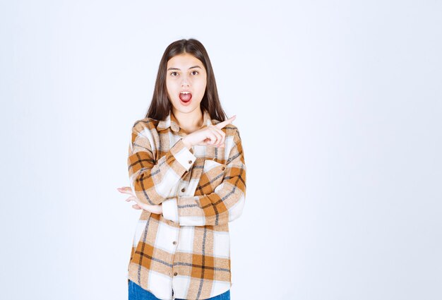  young beautiful woman pointing at somewhere on white wall. 