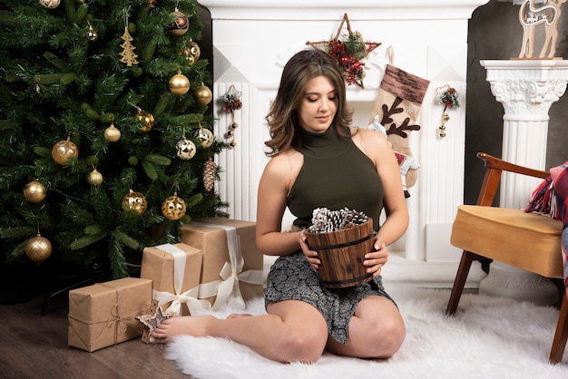 Young beautiful woman posing with basket of pinecones near the Christmas tree