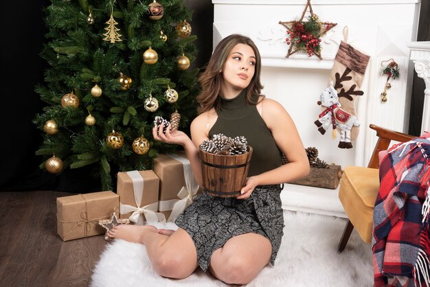 Young beautiful woman posing with basket of pinecones near the Christmas tree