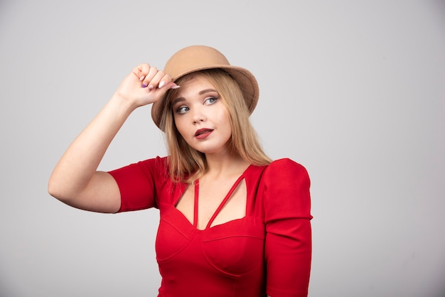 Young beautiful woman in red dress touching her hat.