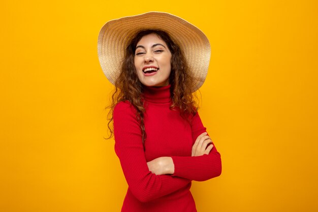 夏の帽子の赤いタートルネックの若い美しい女性は、広く幸せで陽気な笑顔に見えます