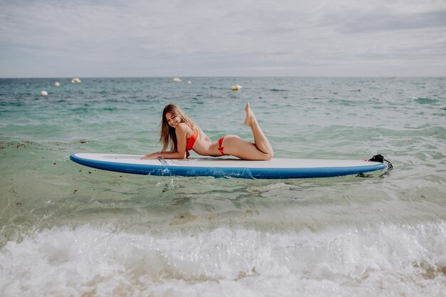 SUPボードで海でリラックスした若い美しい女性。
