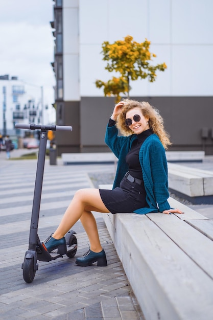 Free photo young beautiful woman riding an electric scooter to work, modern girl, new generation, electric transport, ecology, ecological transport, sunset