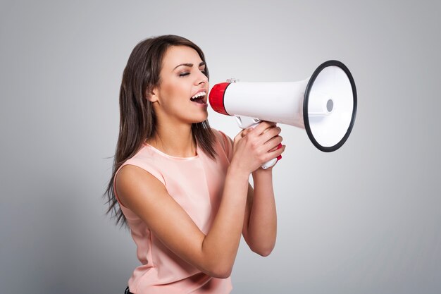 Young beautiful woman screaming by megaphone