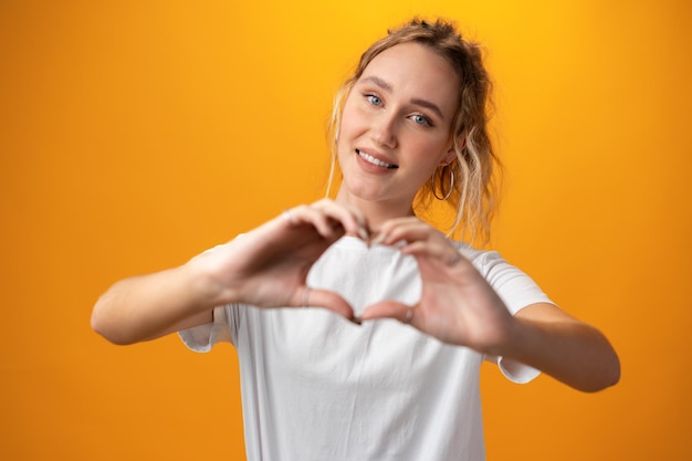 Young beautiful woman showing heart symbol over yellow background