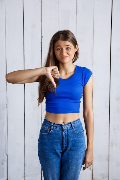 Young beautiful woman showing thumb down dislike over white wooden wall.