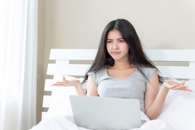 Young beautiful woman sitting on bed, She use slaptop and feel serious and sadly