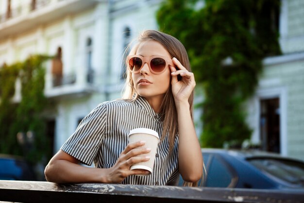 Young beautiful woman sitting on bench, holding coffee.