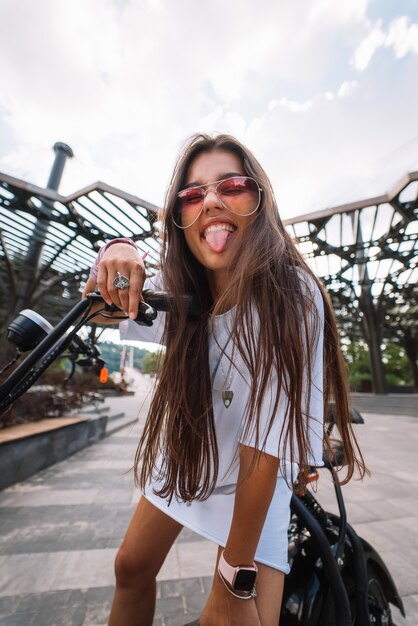 Young beautiful woman sitting on electric scooter and showing tongue