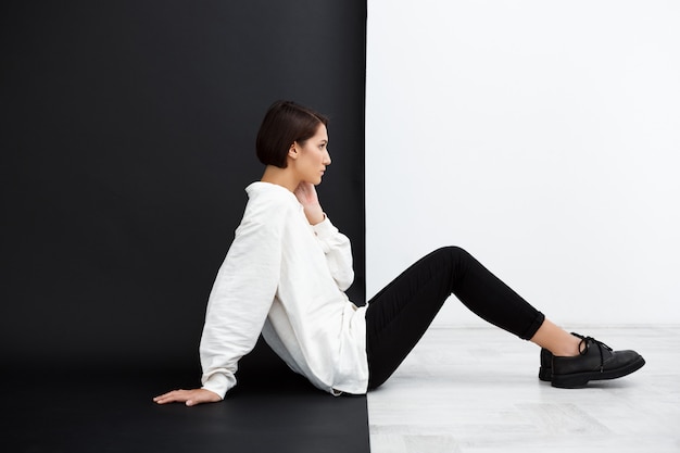 Free photo young beautiful woman sitting on floor over black and white surface